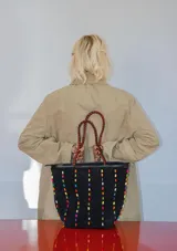 Cartera tipo tote de gamuza color marrón, con correas trenzadas y detalle de piedras naturales incrustadas en líneas verticales. Cuenta con cierre metálico y forro interior de tela.