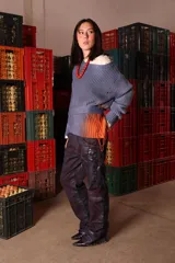 Pantalón de denim de algodón con silueta amplia y construcción estructurada. Presenta un acabado artesanal con efecto de lavado irregular en tonos azul y violeta, destacando un estampado geométrico en una de las piernas y un ruedo con vuelta en color rojo contrastante.