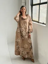 Vestido largo de lino color camel con estampado floral en tonos marrón y crudo, cuello drapeado y mangas largas holgadas.