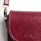 Mini cartera bandolera de cuero, de formato compacto y diseño atemporal con solapa frontal y costuras artesanales decorativas en el borde. Cuenta con el logotipo de la marca grabado en la parte delantera y correa larga regulable.