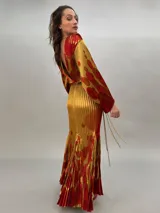 Vestido largo plisado con estampado abstracto en tonos rojo, naranja y dorado, cuello alto y mangas acampanadas. Incluye lazo fino para ajustar en la cintura.