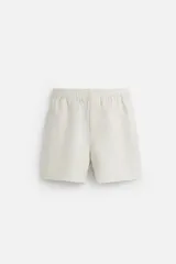 Bermuda relaxed fit confeccionada en tejido ligero de cáñamo. Presenta cintura elástica ajustable con cordón interior, bolsillos laterales y un bolsillo trasero de plastrón con solapa.