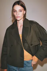 Trench corto Zara Woman Collection confeccionado en hilatura con algodón, en color verde militar. Presenta cuello solapa, manga larga con trabillas y botones en los puños, bolsillos delanteros, bajo asimétrico y cierre frontal cruzado con botones.