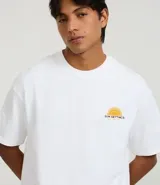 Remera de algodón blanca, corte relajado (relaxed fit), con cuello redondo y manga corta. Presenta un pequeño estampado frontal en el pecho con un sol estilizado y el texto "Sun Settings".