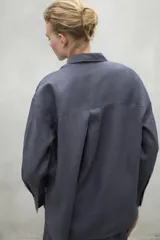 Camisa de corte holgado confeccionada en lino, con cuello clásico, cierre frontal de botones y mangas largas con puños sencillos.