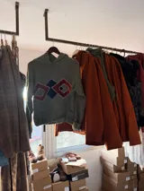 Canguro de lana merino color azul, con capucha y diseño de rombos geométricos en el frente realizados con apliques de terciopelo bordados a mano.