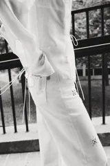 Pantalón de jean blanco, tiro superalto, con piernas amplias y corte holgado. Presenta tachas decorativas en forma de estrella o copo de nieve distribuidas por toda la prenda.