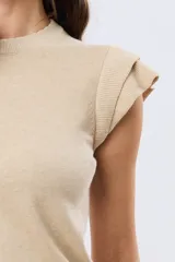 Remera tejida de algodón en color beige, de cuello redondo, sin mangas y con detalles de volados estructurados en los hombros.