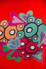 Remera roja de mangas largas con estampado abstracto de círculos y corazones en tonos celeste, verde, naranja y rosa.