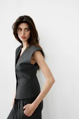 Chaleco de sastre con escote en V, cierre frontal con botones y diseño de hombros caídos. Presenta un estampado de raya diplomática sobre fondo gris oscuro.