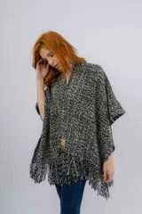 Ruana artesanal tejida en telar manual, con diseño jaspeado en tonos negro y crudo. Presenta una textura rústica y terminación con flecos en el ruedo, además de una etiqueta de cuero con la marca Pura Lana.