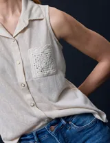 Blusa color crema sin mangas, con cuello camisero, cierre frontal con botones y bolsillo de crochet.