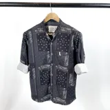 Camisa negra de cuello mao con estampado de arabescos en blanco y logo de la marca bordado en el pecho. Mangas largas con puños abotonados y corte clásico.