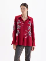 Camisa de manga larga color rojo, con cuello clásico y cierre frontal de botones. Presenta un estampado artístico que combina motivos florales en tonos rosados con ilustraciones de alfileres de gancho.