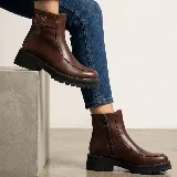 Bota corta de cuero color marrón con suela track negra, cierre lateral y detalle de tira con hebilla en la parte superior.
