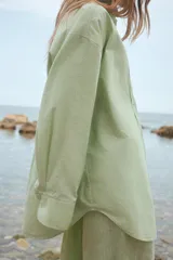 Camisa oversize de cuello solapa, manga larga con puño caído y bolsillo de plastrón en el pecho. Presenta un patrón de rayas verticales sutiles en tono verde lima.