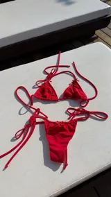 Conjunto de bikini rojo con corpiño triangular con delicados moños en los tirantes y bombacha semivedetina con lazos laterales ajustables y detalle de moño en el frente.
