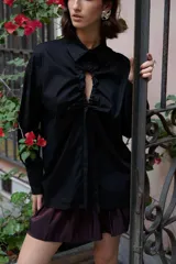 Camisa oversize de manga larga en color blanco, confeccionada en algodón. Presenta cuello clásico, puños abotonados y una abertura central ovalada con jaretas ajustables que permiten fruncir la prenda.