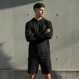 Canguro deportivo negro con capucha, confeccionado en tejido técnico elástico. Presenta un pequeño logo en el pecho, un bolsillo con cierre en la manga izquierda y detalles estampados en la manga derecha.