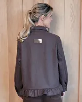 Sobrecamisa de pana color marrón oscuro, con cuello camisero, cierre frontal de botones y detalle de volado en el ruedo. Presenta mangas largas con puños y bolsillos frontales aplicados.