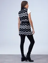 Chaleco largo tejido con cuello solapa, bolsillos delanteros, pasadores en la cintura y lazo para ajustar. Diseño con patrón de zigzag en blanco y negro.