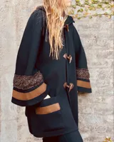 Saco tipo capa color negro, tejido en lana merino con capucha y cierre con broches tipo tanca de cuero. Presenta detalles de cintas tejidas en puños y bolsillos.