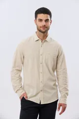 Camisa de lino de manga larga en color beige, con cuello camisero, cierre frontal de botones y un bolsillo ojal en el pecho.