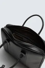 Maletín de cuero negro con acabado abatanado, cierre de cremallera, doble asa de mano, asa de hombro ajustable y extraíble, bolsillo interno para dispositivos electrónicos de hasta 13 pulgadas y detalle de candado. Marca Mango.