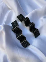 Par de aros colgantes con forma geométrica irregular, recubiertos de strass negros sobre base plateada.