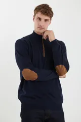 Sweater de punto gris con medio cierre frontal, cuello alto y coderas en tono marrón. Presenta un diseño clásico con puños y ruedo acanalados.