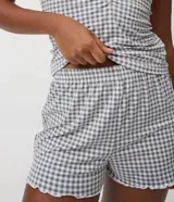 Pijama corto de dos piezas de la marca Lov, confeccionado en tejido peach touch de poliéster y elastano. Incluye una remera de manga corta con escote redondo, detalle de frunce en el busto y terminaciones con volados, acompañada de un short con cintura elástica y diseño estampado a cuadros vichy en tonos gris y blanco.