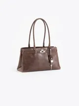 Cartera tipo shopper de cuero vacuno marrón, con silueta estructurada, doble asa de hombro y herrajes metálicos plateados. Incluye tira decorativa con candado y llave colgantes.