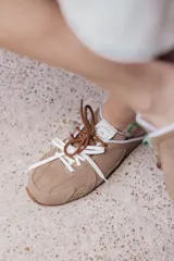 Zuecos de cuero color beige, con cordones marrones y verdes, y detalles de costuras.