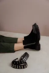 Bota corta de cuero gamuzado color marrón chocolate, con punta cuadrada y suela track. Presenta una correa con hebilla desmontable y cierre lateral con cremallera.