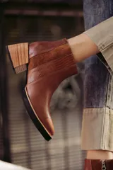 Bota corta de cuero color marrón, con taco de madera y suela negra. Presenta un diseño con paneles combinados: cuero liso, gamuza y un panel con textura de piel de cocodrilo en relieve.