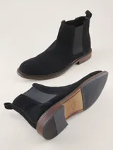 Bota Chelsea de gamuza gris con elásticos laterales, suela de goma marrón y tirador trasero.