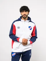 Campera deportiva Umbro del Club Nacional de Football, con cierre frontal, capucha ajustable con cordones y diseño en bloques de color azul, celeste y blanco. Presenta el logo de la marca y el escudo del club bordados en el pecho.