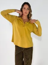 Remera de manga larga color mostaza, con cuello polo y cierre frontal de botones. Confeccionada en algodón, presenta un diseño holgado y casual.