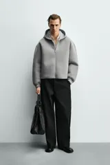 Sudadera gris de corte boxy fit con capucha y cierre frontal de cremallera. Confeccionada en tejido doble y compacto, cuenta con bolsillos laterales ocultos en la cadera y mangas largas con puños elásticos.