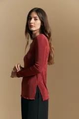 Top de manga larga con textura suave y leve brillo. Presenta una silueta al cuerpo, tajos laterales y terminaciones onduladas en el ruedo.