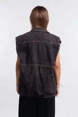 Chaleco de denim negro con efecto deslavado, diseño sin mangas, bolsillos frontales con solapa, costuras en contraste y botones metálicos.