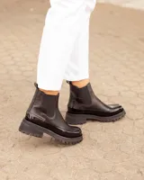 Botinetas tipo Chelsea de cuero negro, con paneles laterales elásticos y suela track dentada de goma. Presentan una combinación de texturas entre cuero mate y cuero charolado en la puntera y el talón.