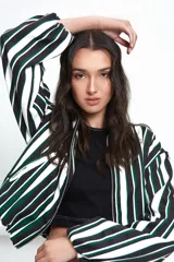 Campera tipo bomber corta, con cierre frontal, cuello a la base, bolsillos ojal y mangas largas abullonadas. Presenta un diseño estampado a rayas verticales en tonos blanco, negro y verde.