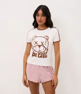 Pijama corto Lov de dos piezas confeccionado en peach touch. Compuesto por remera blanca de manga corta con ribetes y cuello marrón, con estampa frontal de oso y la leyenda "Be Cool", y short de rayas verticales rosadas y blancas con cintura elastizada.