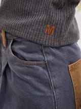 Camiseta negra de manga larga, con tejido acanalado, cuello redondo a la base y corte tipo crop. Presenta costuras rojas a la vista y un logo "M" bordado en rojo en el lateral izquierdo.