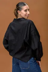 Camisa negra de corte clásico con mangas largas abullonadas y puños abotonados. Presenta paneles de encaje floral en la parte superior delantera y trasera, combinando texturas con un diseño elegante y sofisticado.