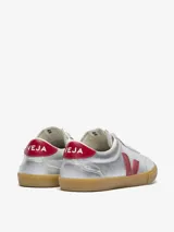 Championes Veja modelo Volley, de color plateado metalizado con detalles en rojo en el logo lateral y el talón. Presenta suela de goma color caramelo y cordones blancos.