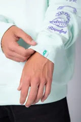 Buzo oversize de cuello redondo en color verde menta, confeccionado en tela rústica. Presenta un pequeño estampado en el pecho y una serie de estampados verticales a lo largo de la manga izquierda.