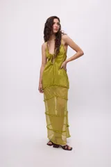 Vestido largo de chiffon color verde lima con acabado brillante. Presenta un diseño de tirantes finos con escote regulable mediante lazo frontal, corte holgado y falda con múltiples recortes horizontales decorados con volados.