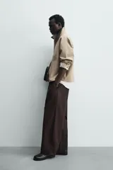 Sobrecamisa de corte relajado color beige, con cuello solapa en efecto piel de color negro. Presenta cierre frontal con cremallera, bolsillos de vivo en la cadera y mangas largas con puños ajustables.